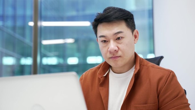 自信的亚洲商人在商务办公室的工作场所坐着，正在用笔记本电脑打字。