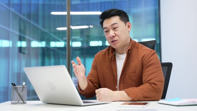 自信的亚洲商人在现代办公室的工作场所使用笔记本电脑进行视频通话。