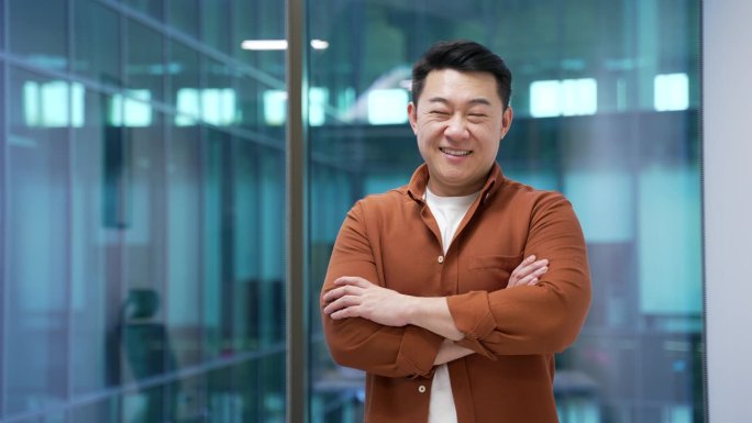 一位快乐的亚洲商人在现代商务办公室的工作场所双臂交叉站立。