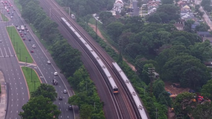 从空中俯瞰两列长岛铁路列车在阴天行驶。无人机镜头向下倾斜，推进并向上倾斜以跟随驶向纽约市的列车。