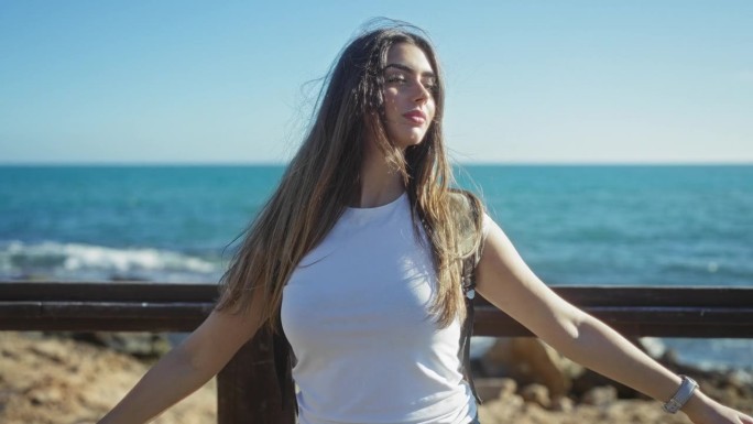 女人在阳光明媚的海滨长廊上享受着蓝色的海洋和天空，拥抱自由与自然，沉浸在宁静的城市风景中。