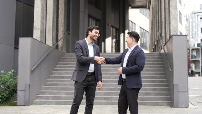 两位商人在现代办公大楼外握手，象征着成功的商业伙伴关系和团队合作。