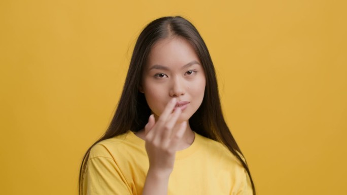 亚洲女性摆姿势，触碰嘴唇，玩弄头发，黄色背景。