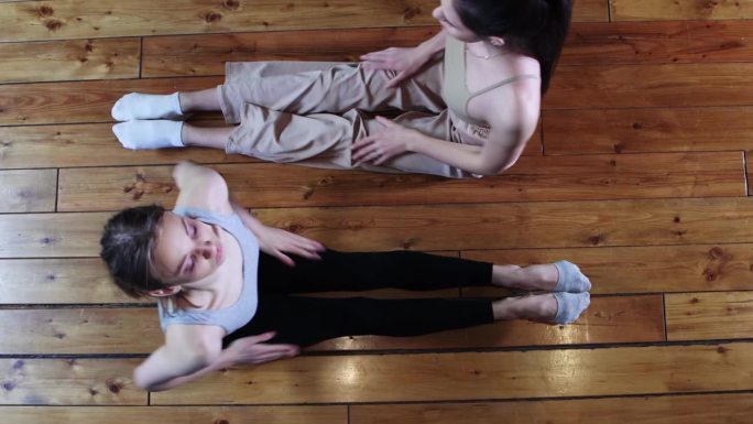 两位瘦弱的女性在健身房一起训练 - 坐在地板上向前倾身。