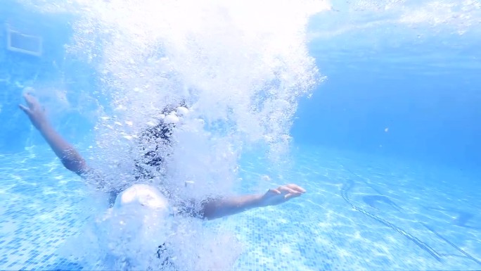 有趣的孩子游泳，从池边跳入水中，慢动作潜入水下。