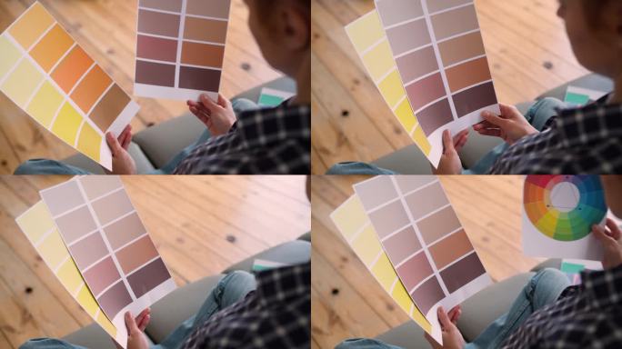 无法辨认的白人女性背影坐在沙发上，手持选择颜色的图表，展示多种色彩模板，进行房屋装修样本的选择，设计