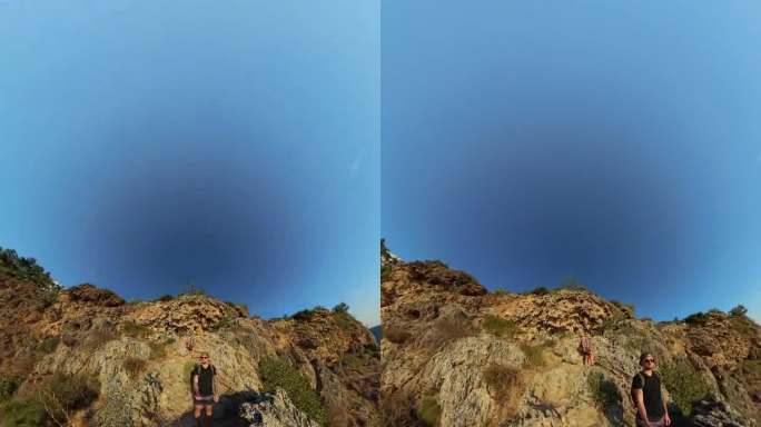 竖屏视频。两个人站在悬崖上，周围是崎岖的地形和海洋，采用球形全景拍摄，宽阔的视野展现地平线。