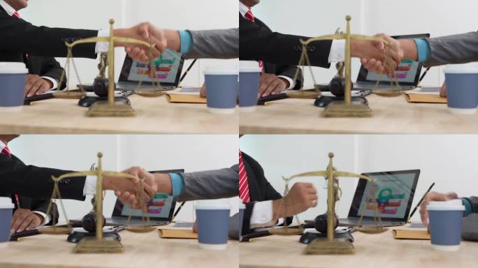 男性律师与坐在桌子旁的男性客户握手，桌上有法官的槌子和天平。法律协议概念。