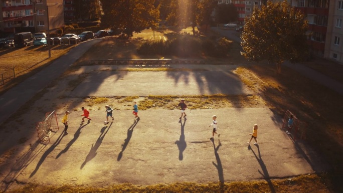 航拍镜头：多元文化的朋友们在阳光明媚、天气完美的后院踢足球。快乐的男孩和女孩们在户外的足球场上享受运