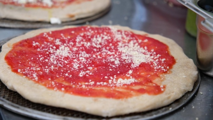 特写：披萨店里，双手在披萨饼底上撒上帕玛森芝士，铺上大块的芝士。烘烤前正宗意大利披萨的制作过程。