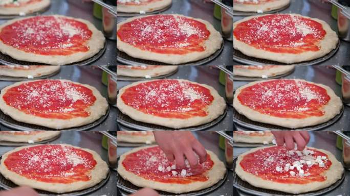 特写：披萨店里，双手在披萨饼底上撒上帕玛森芝士，铺上大块的芝士。烘烤前正宗意大利披萨的制作过程。