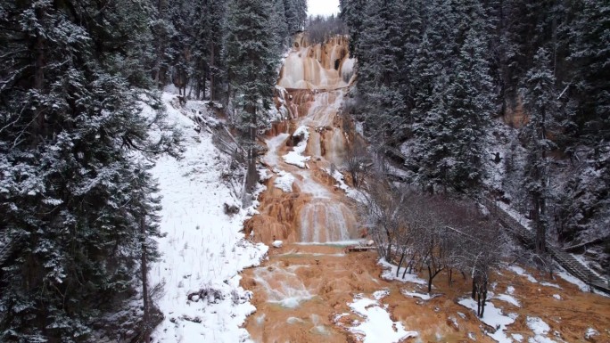 无人机视角拍摄的中国四川松潘牟尼沟扎嘎瀑布。冬季晴天，白雪覆盖的松林与美丽的瀑布。4K实时摄像，旅行