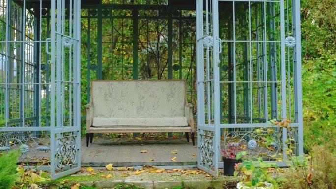 秋日花园里，华丽的凉亭结构，配有空置的古董沙发和疯长的植物