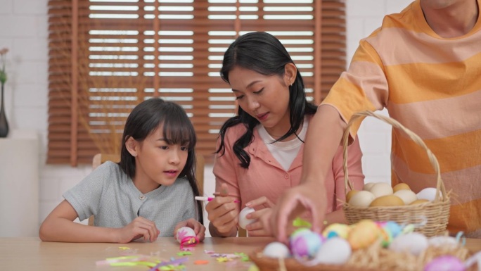 亚洲年轻儿童和父母在家里的桌子上给复活节彩蛋上色。快乐的家庭，可爱的孩子们和爸爸妈妈一起享受在家客厅