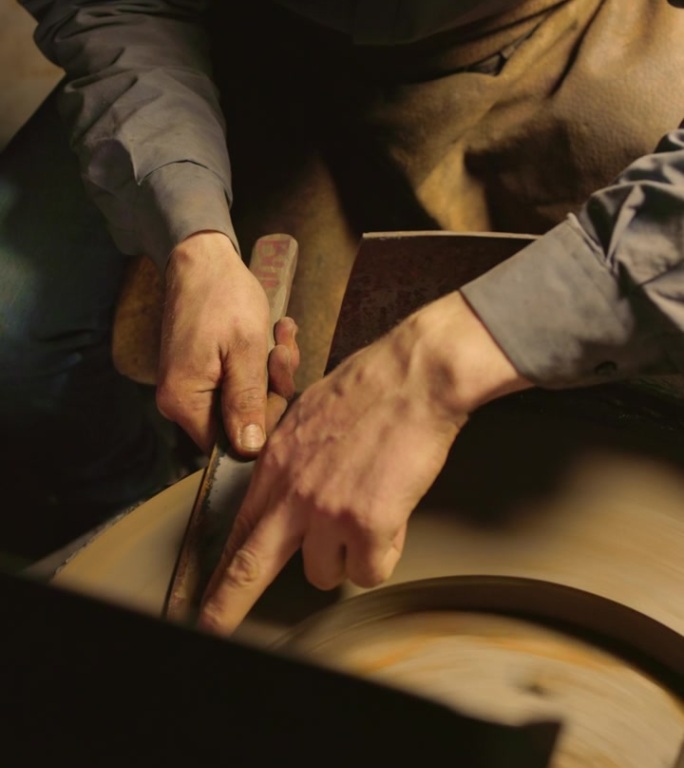 聚焦的铁匠在昏暗的灯光下用湿磨机磨刀。