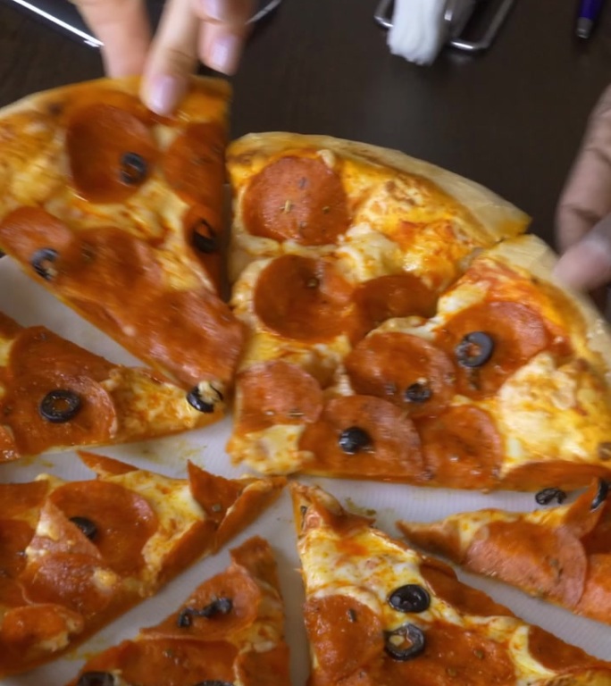 美味的意大利香肠披萨片整齐地摆放在盘子上，手伸向一片披萨。