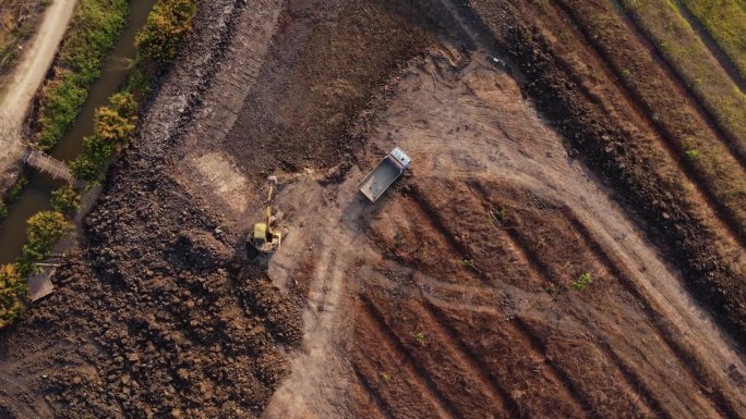 航拍视角：一辆带挖斗的轮式装载挖掘机在建筑工地上将沙子装入重型土方工程车。挖掘机为农业领域挖掘土坑。