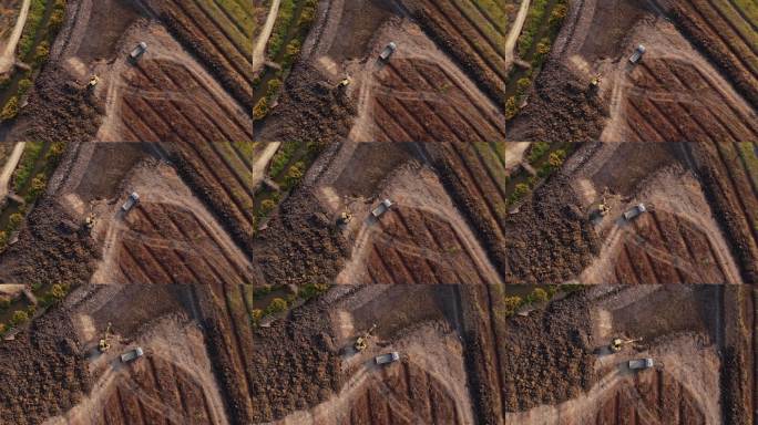 航拍视角：一辆带挖斗的轮式装载挖掘机在建筑工地上将沙子装入重型土方工程车。挖掘机为农业领域挖掘土坑。