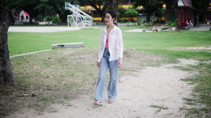 一个年轻的亚洲女性悠闲地漫步在一条小径上，周围是树木和清新的空气。