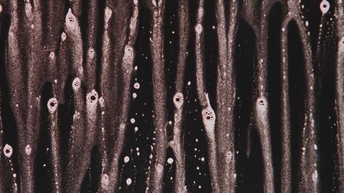 一只手在黑色背景上擦去玻璃表面滴落的泡沫。