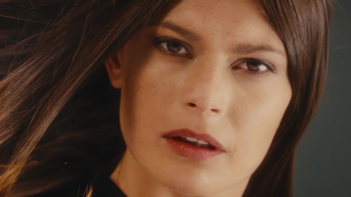 优雅的黑色连衣裙女子在渐变背景上缓慢转身，甩动她那长长的光滑健康的巧克力棕色直发。