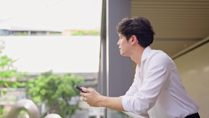 亚洲年轻男商人在城市中站着，使用智能手机聊天。吸引人的英俊男性员工自信地与同事通过手机沟通和讨论。