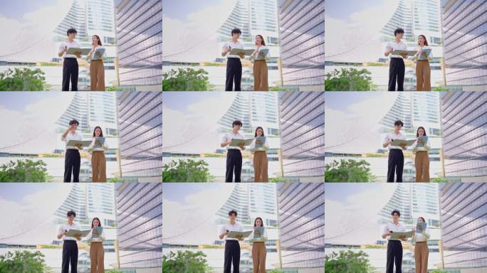 亚洲年轻男女商人伙伴在城市户外工作。吸引人的情侣员工在公司办公室外自信地站着，感到快乐和放松，享受闲