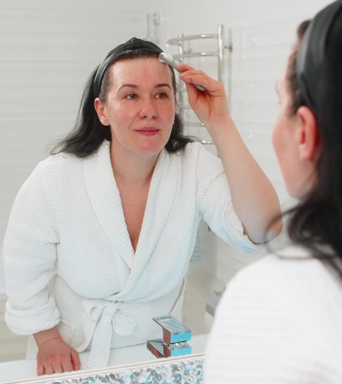 中年成熟的女性在家中轻柔地用微针滚轮按摩面部，享受放松的护肤疗程。