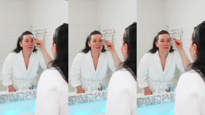 中年成熟的女性在家中轻柔地用微针滚轮按摩面部，享受放松的护肤疗程。